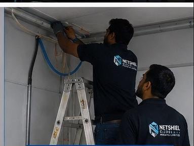 Two technicians running overhead cabling from a ladder